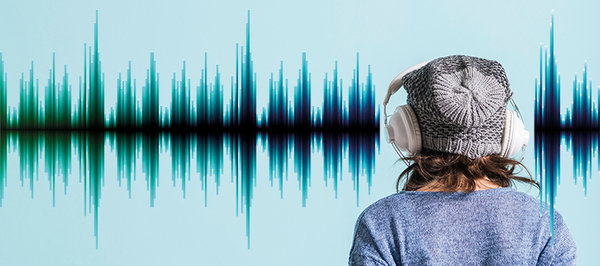 Person mit Mütze und Kopfhörer von hinten vor einer Wand mit Audio-Pegel-Darstellung