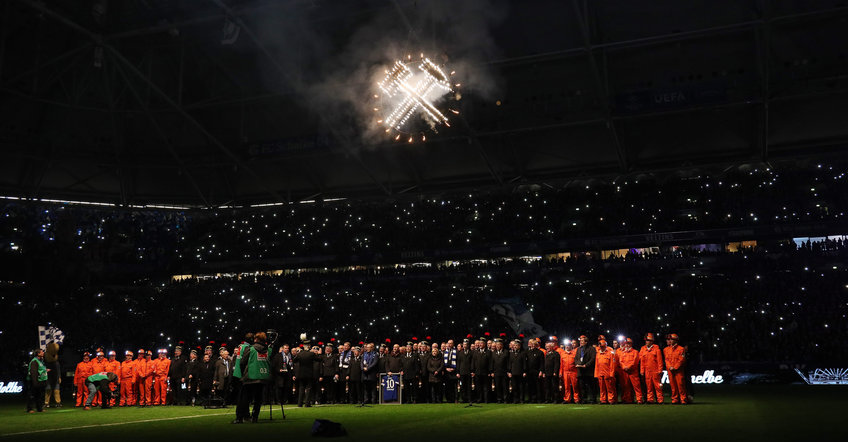 Miners stand on the pitch in the Schalker Arena before the game; hammer and pick are shining above them. 